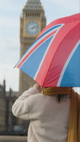 Vertikales-Video-Einer-Frau-Im-Urlaub,-Die-Ein-Foto-Von-Parlamentsgebäuden-In-London,-Großbritannien,-Unter-Dem-Schirm-Von-Union-Jack-Macht